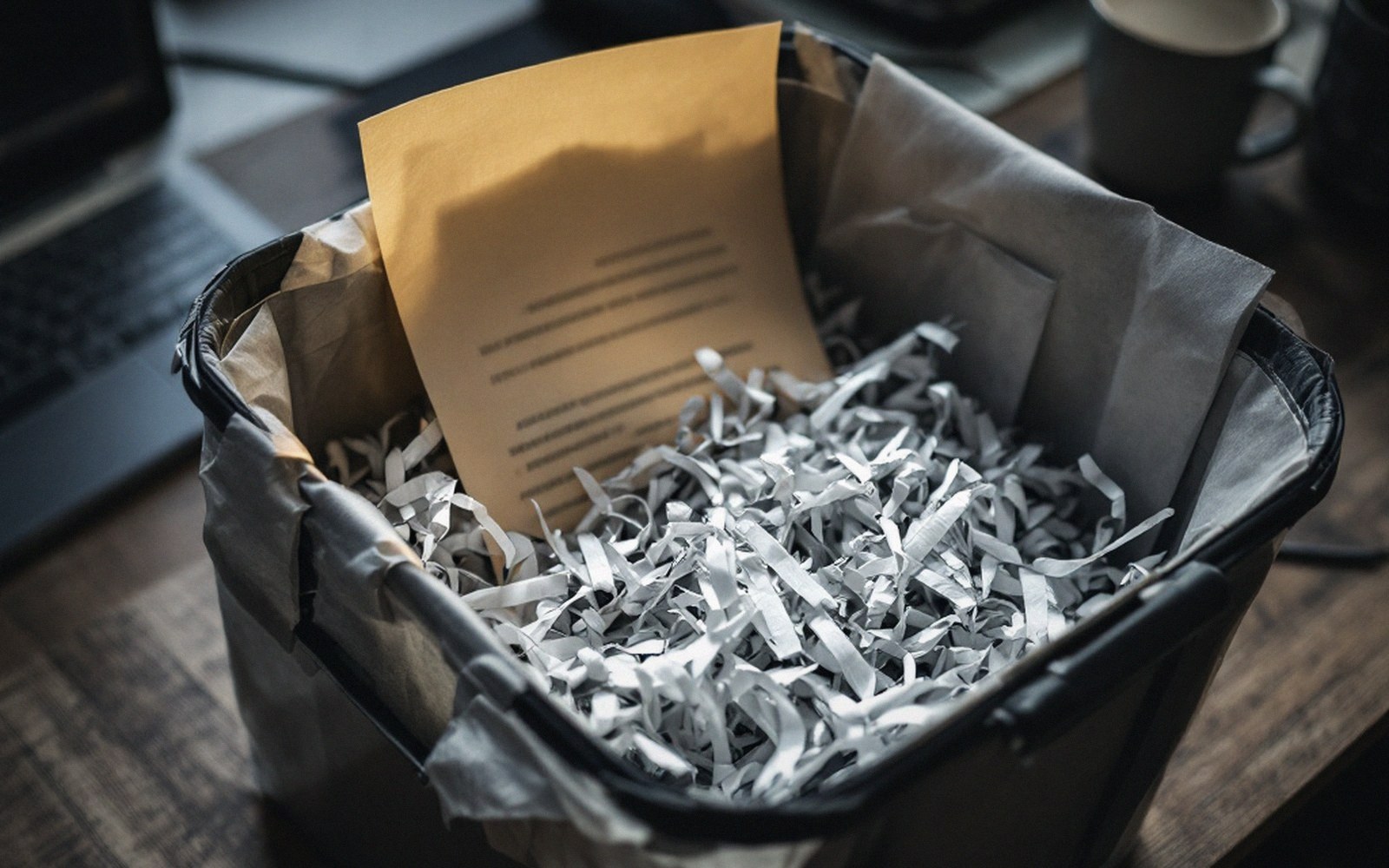 A shredded paper document in a bin beside a desk, cold office light