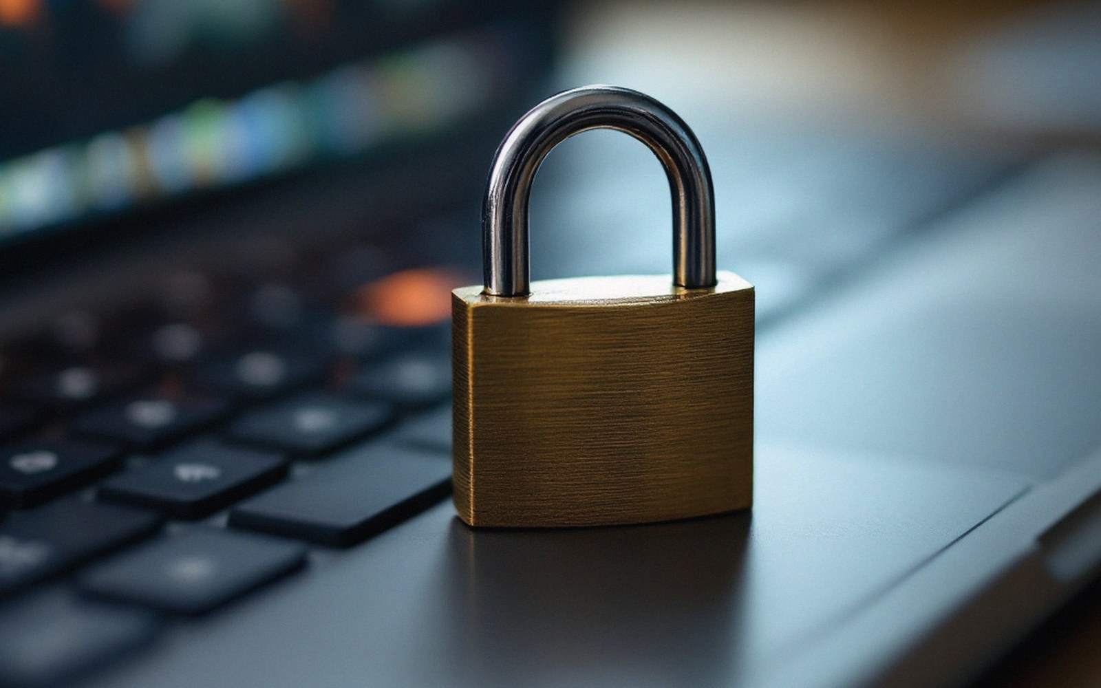 A small brass padlock lying closed on a laptop keyboard, shallow focus, desk light